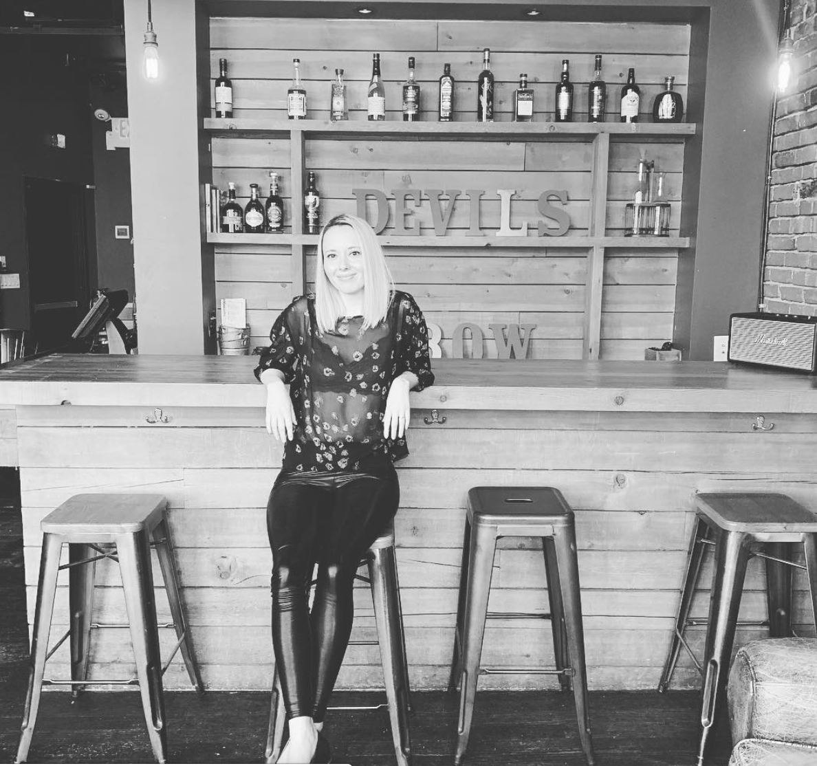 Woman at a bar, smiling, leaning on the wooden counter. 