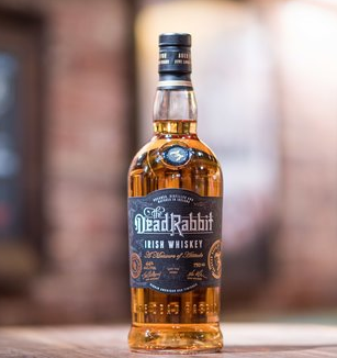 Bottle of Dead Rabbit Irish Whiskey, amber liquid, black label, wooden surface, blurred background.