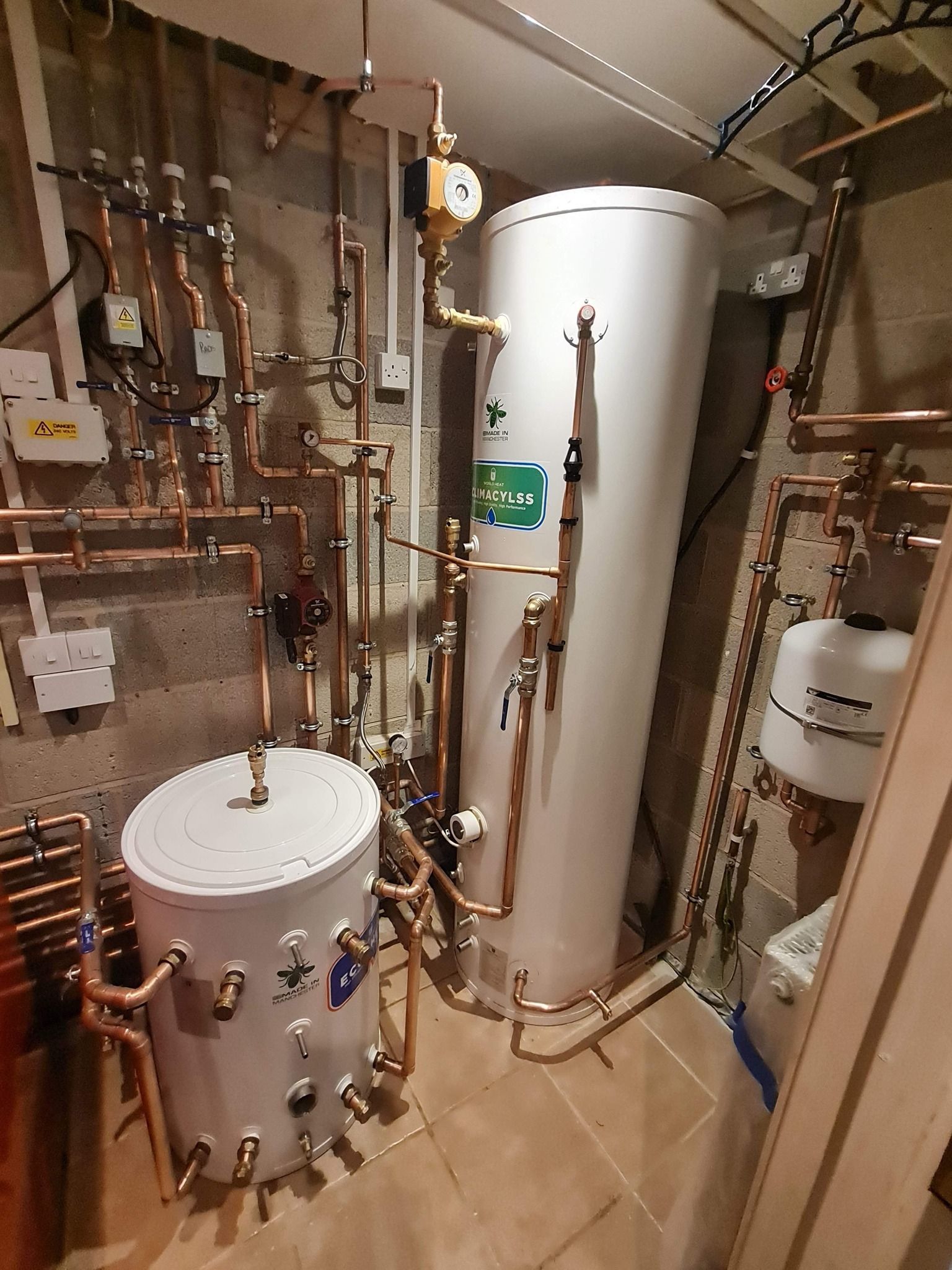 A  boiler room with two water heaters and a lot of pipes.