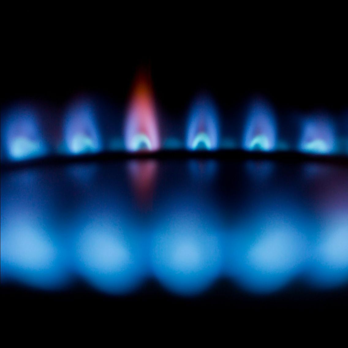 A close up of a boiler burner with blue flames coming out of it.