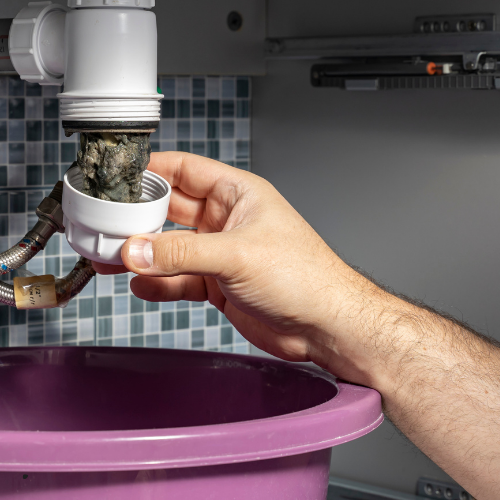 A person is holding a drain pipe over a sink.