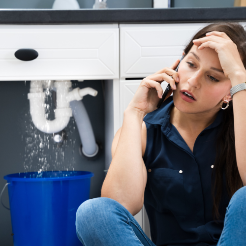 A woman is talking on a cell phone in front of a leaking sink