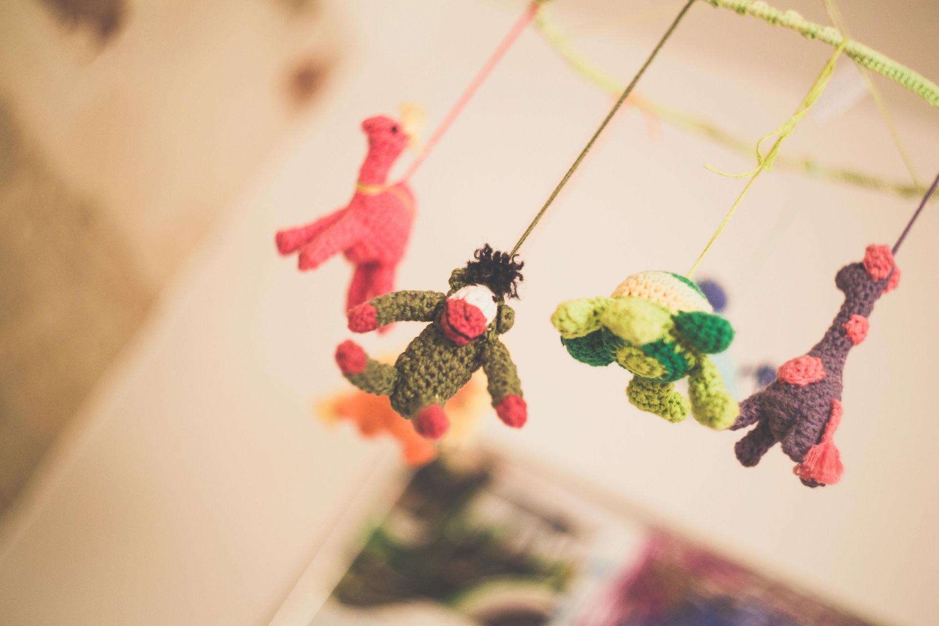 Crocheted dinosaur mobile in soft focus, hanging in a nursery.