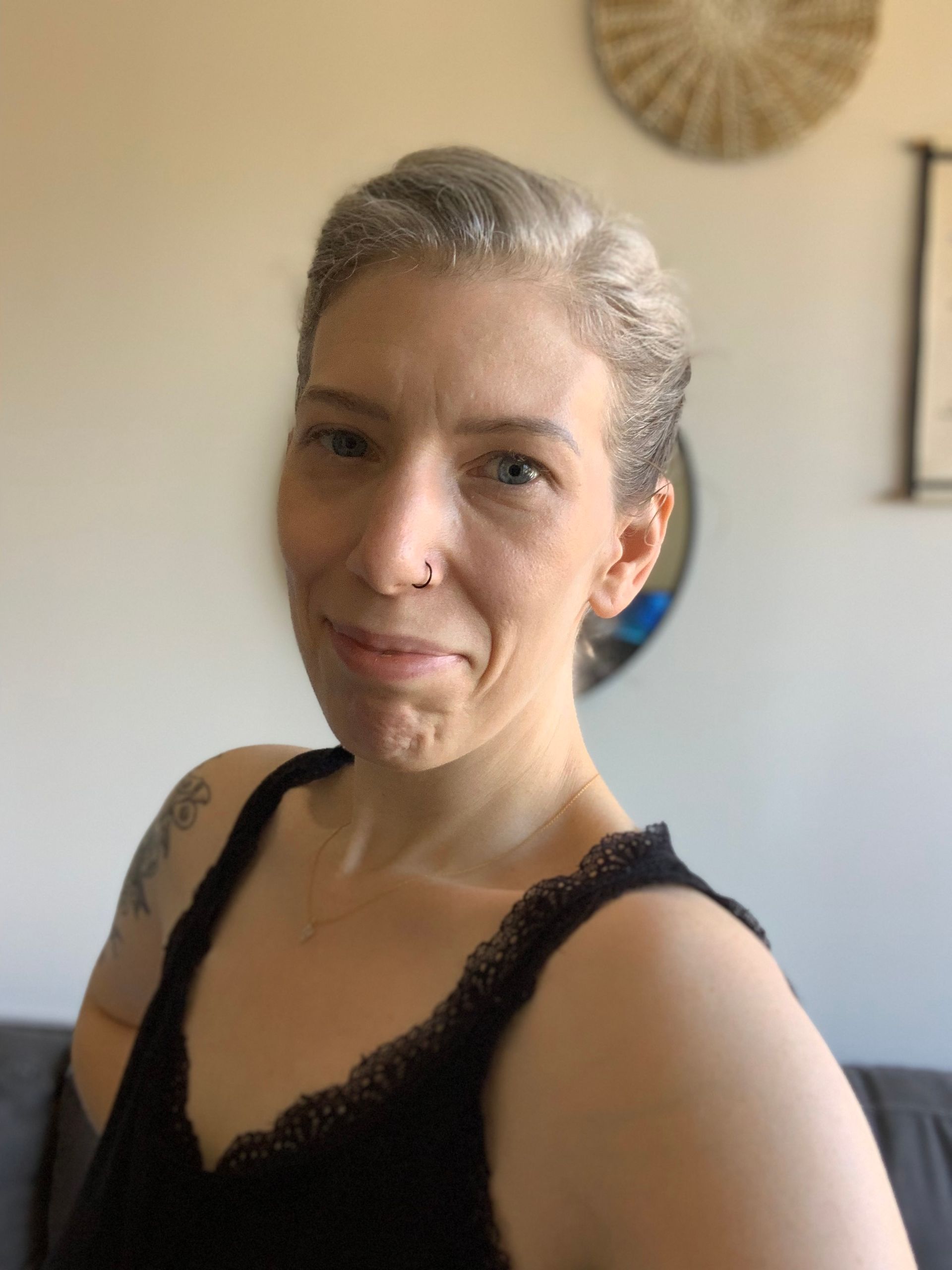 Woman with gray hair smiles, wearing a black top. In a home setting.