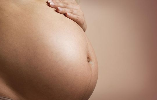 Pregnant belly, hand resting on the abdomen, light skin, neutral background.
