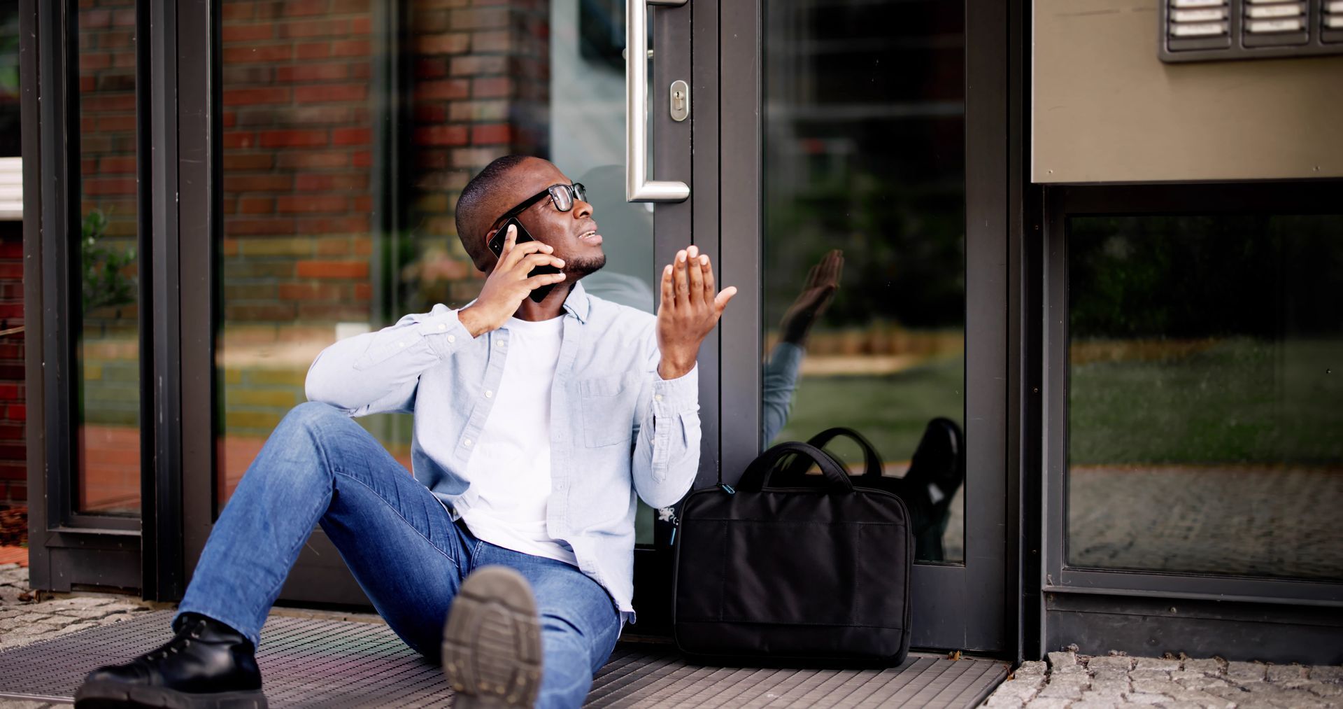 Frustrated African American man locked out of house waiting for locksmith.