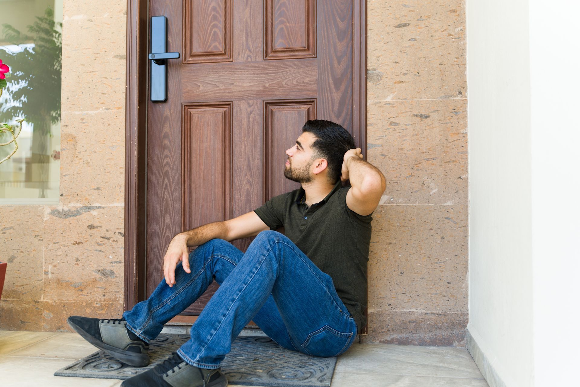 Person sitting on a doorstep in front of a closed wooden door, resting against the doorframe.