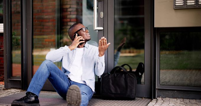 Man on phone locked out of building, seeking help for lockouts with a black briefcase nearby.