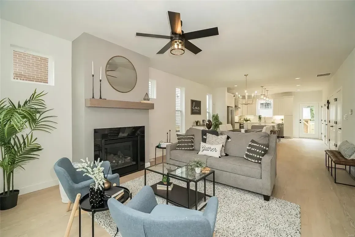 A living room with a couch , chairs , a fireplace and a ceiling fan.