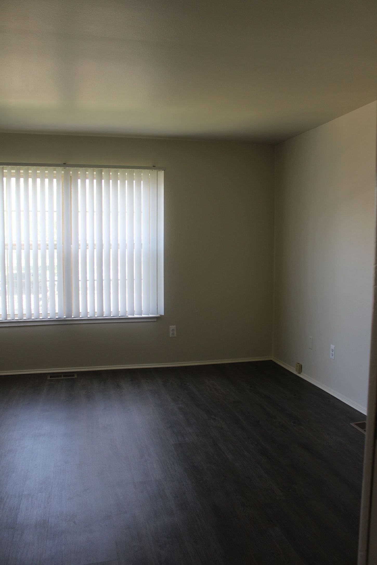 An empty living room with a large window and blinds.