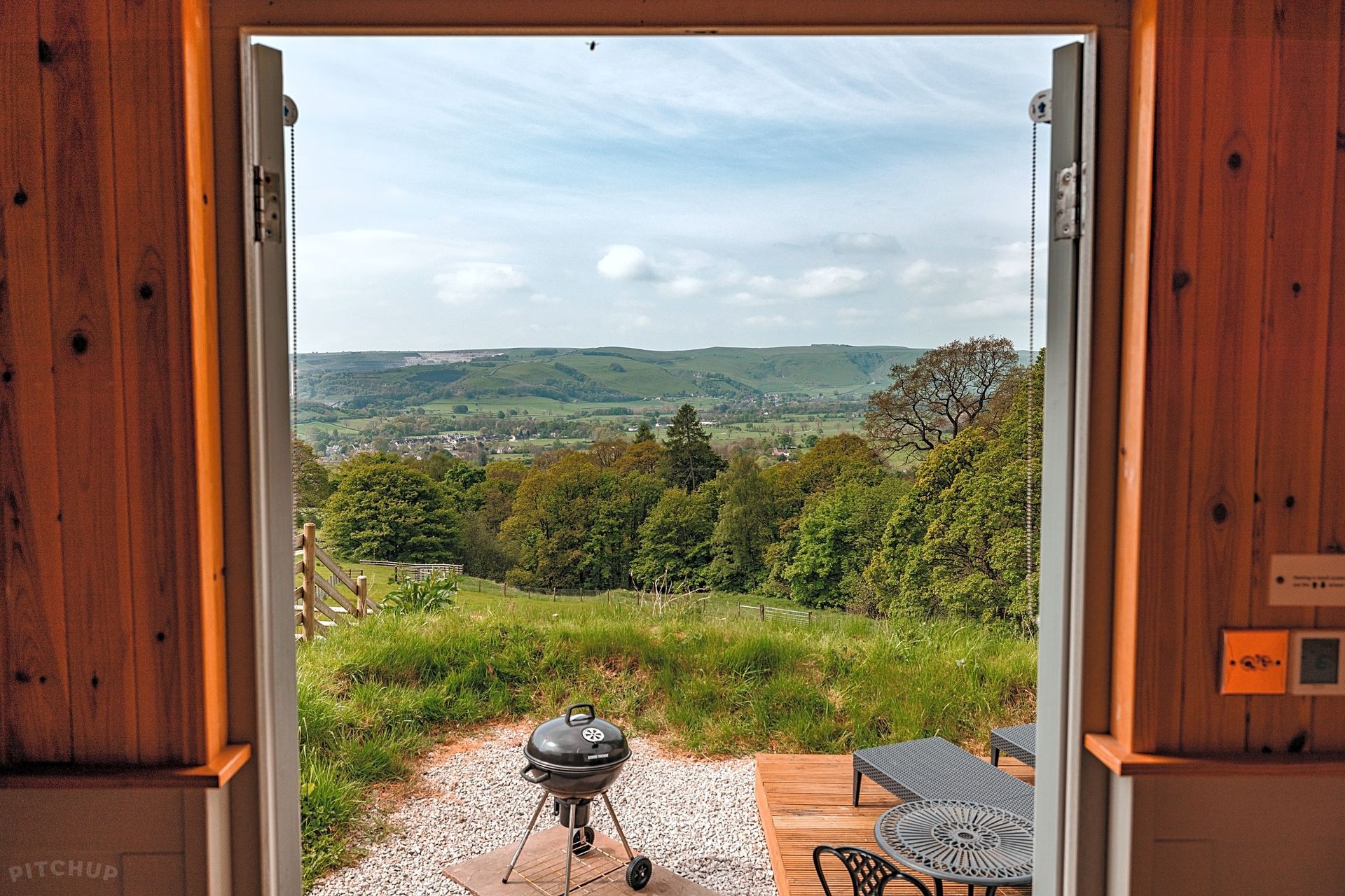 Open doorway to a grassy garden and distant hills, with a patio table and chairs in front