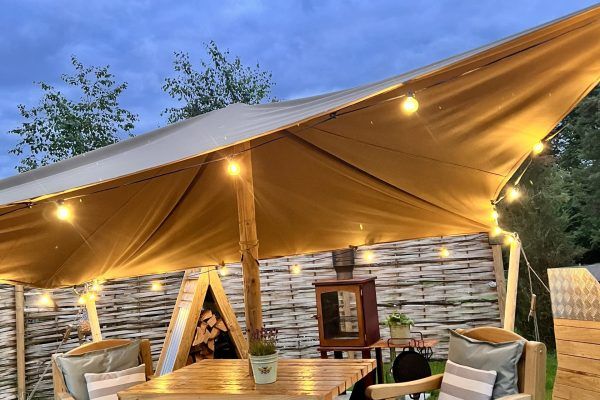 Glowing canvas tent lounge at dusk with wooden seating and warm lights under a peaked canopy