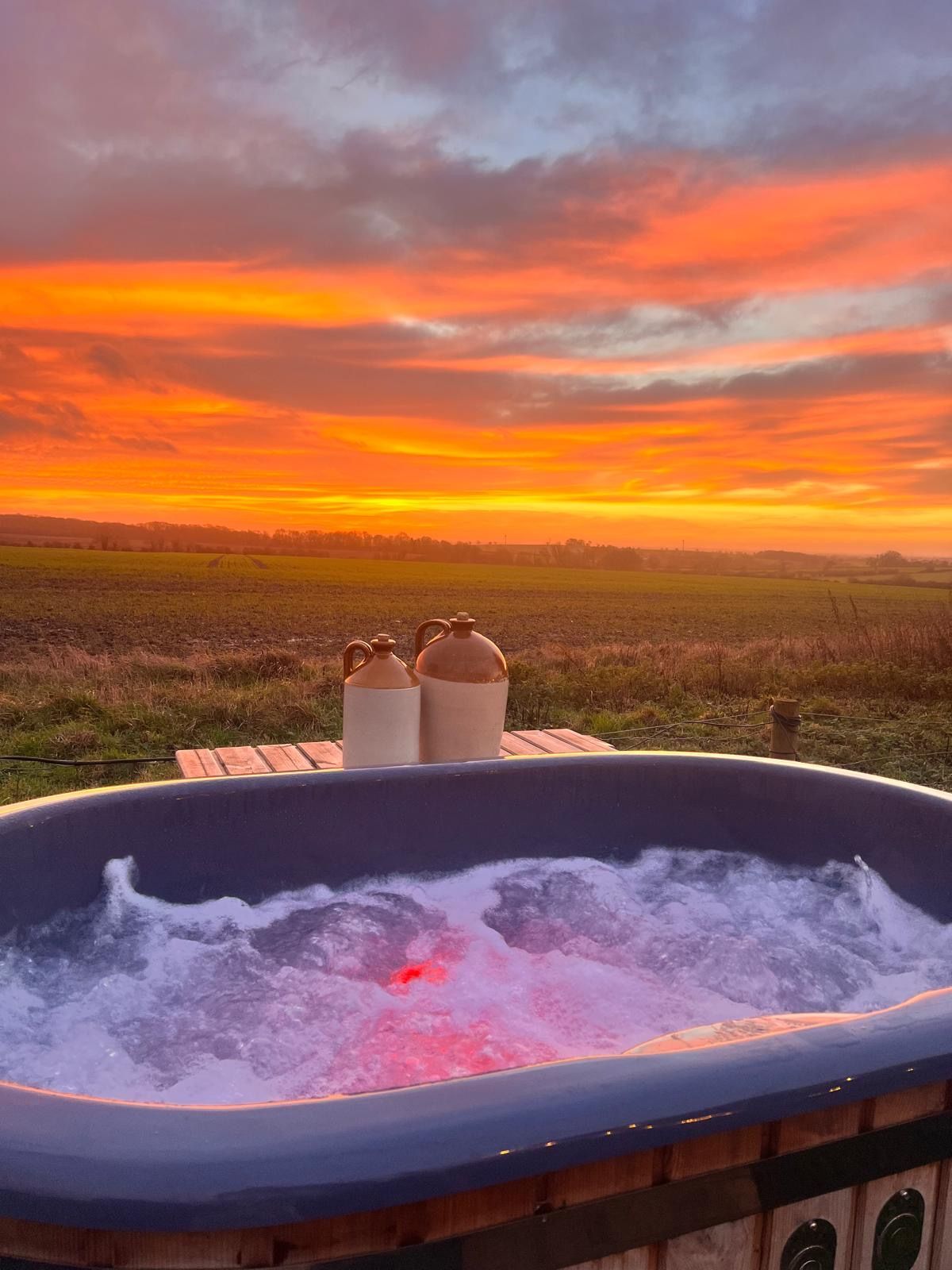 Hot tub with bubbling water at sunset overlooking a grassy field and colorful sky