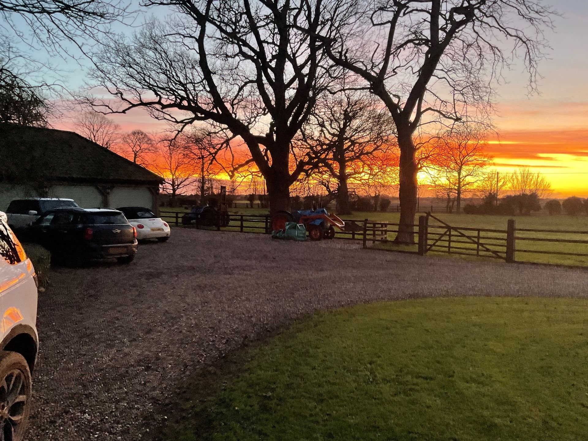 Sunset over a gravel parking area with trees, parked cars, and a glowing orange sky