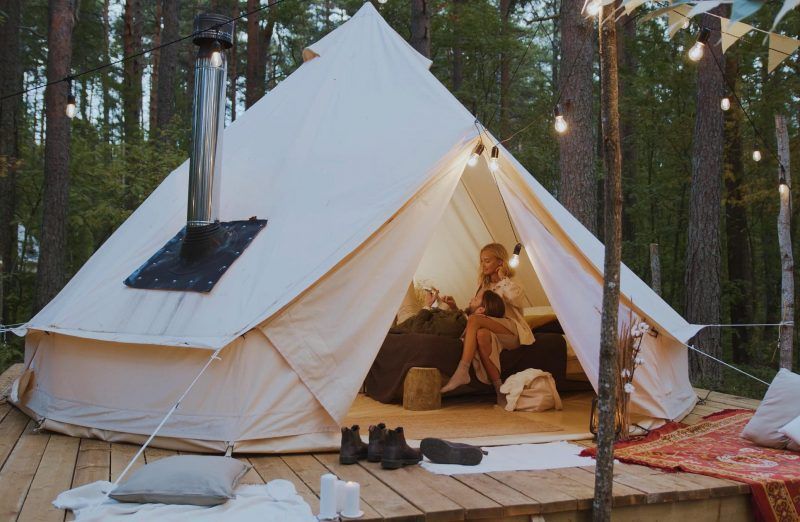 Canvas tent on a wooden deck in a pine forest, with a person sitting inside near the open entrance.