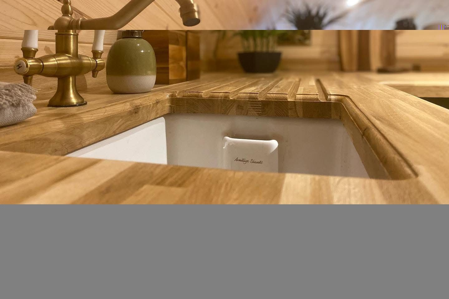Wooden kitchen sink with brass faucet, white basin, and olive soap dispenser on a wood countertop.