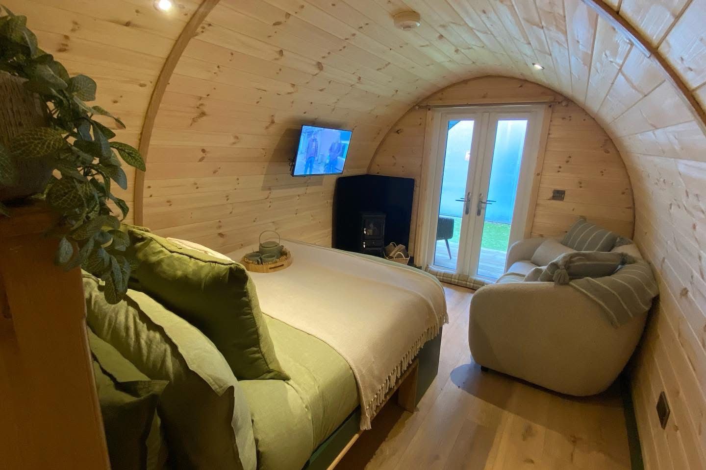 Cozy wooden cabin bedroom with a bed, sofa, TV, and arched door to a green patio