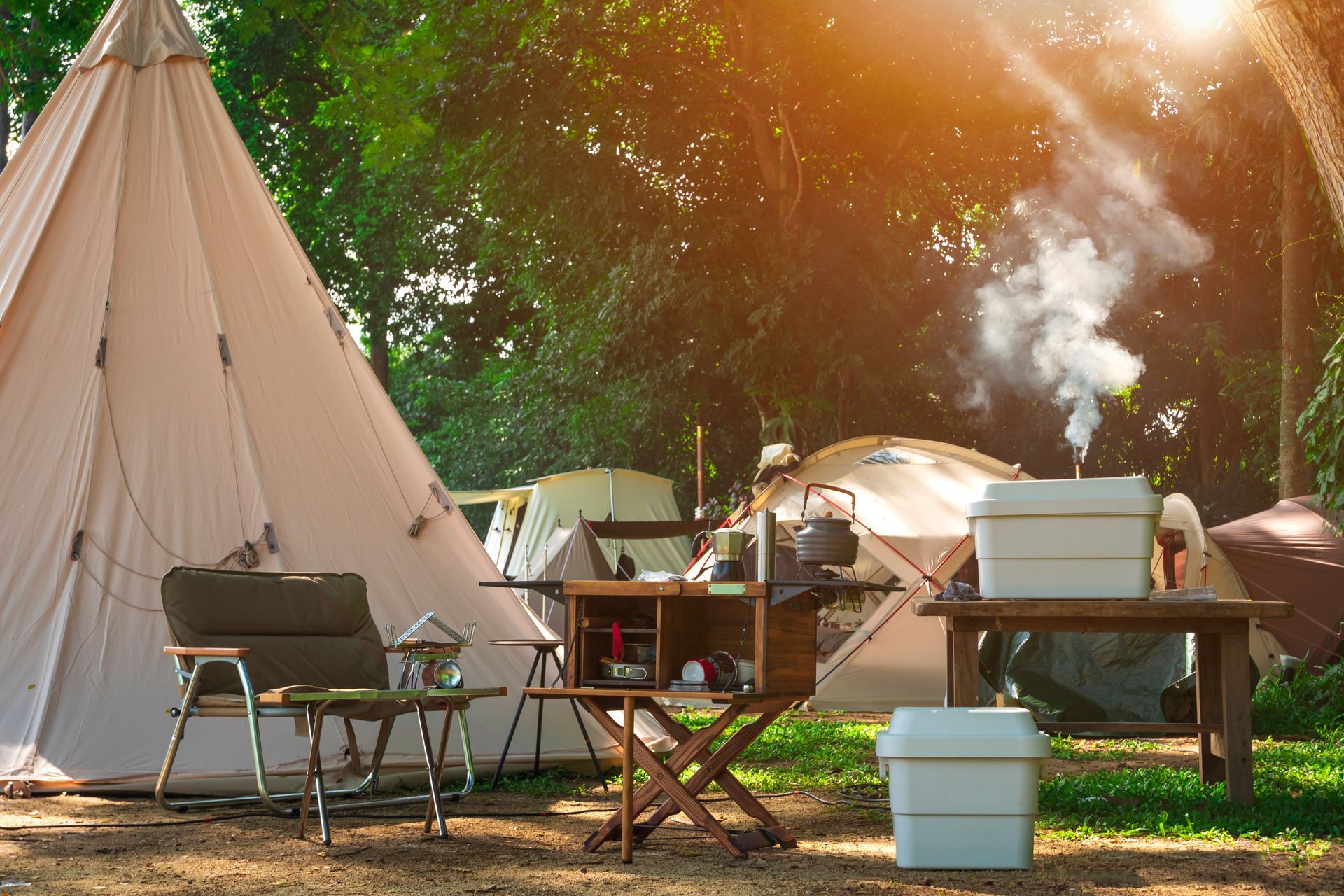 Tent campsite with chairs, tables, and cooking gear in a sunlit wooded area
