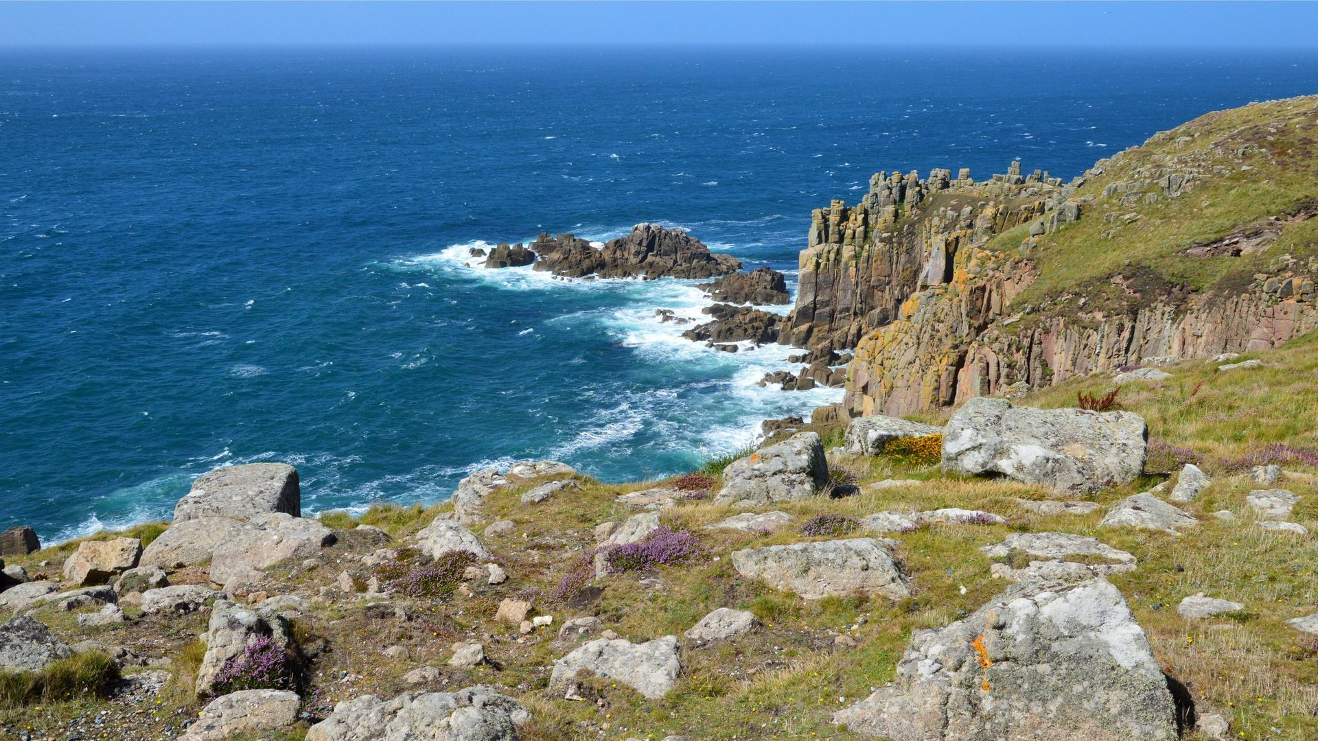 Rocky coastal cliff with blue ocean waves and grassy foreground under a clear sky