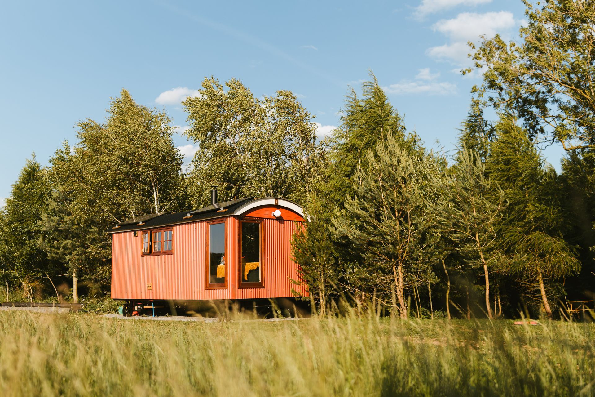 Small orange cabin in a grassy field with trees and blue sky behind it