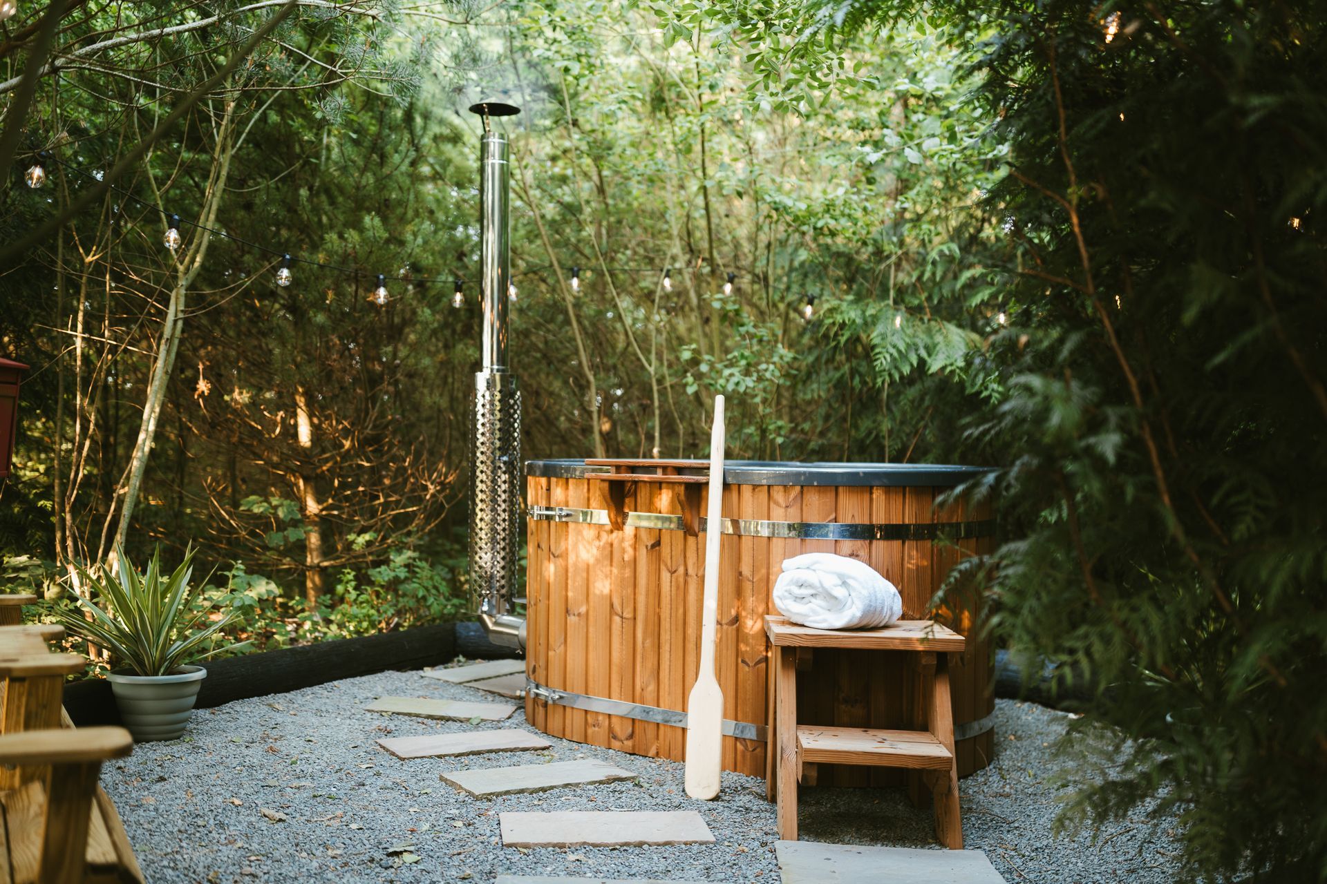 Wooden hot tub on a gravel patio surrounded by lush green bamboo and trees