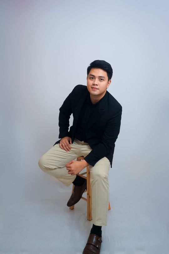 A young man is sitting on a wooden stool.