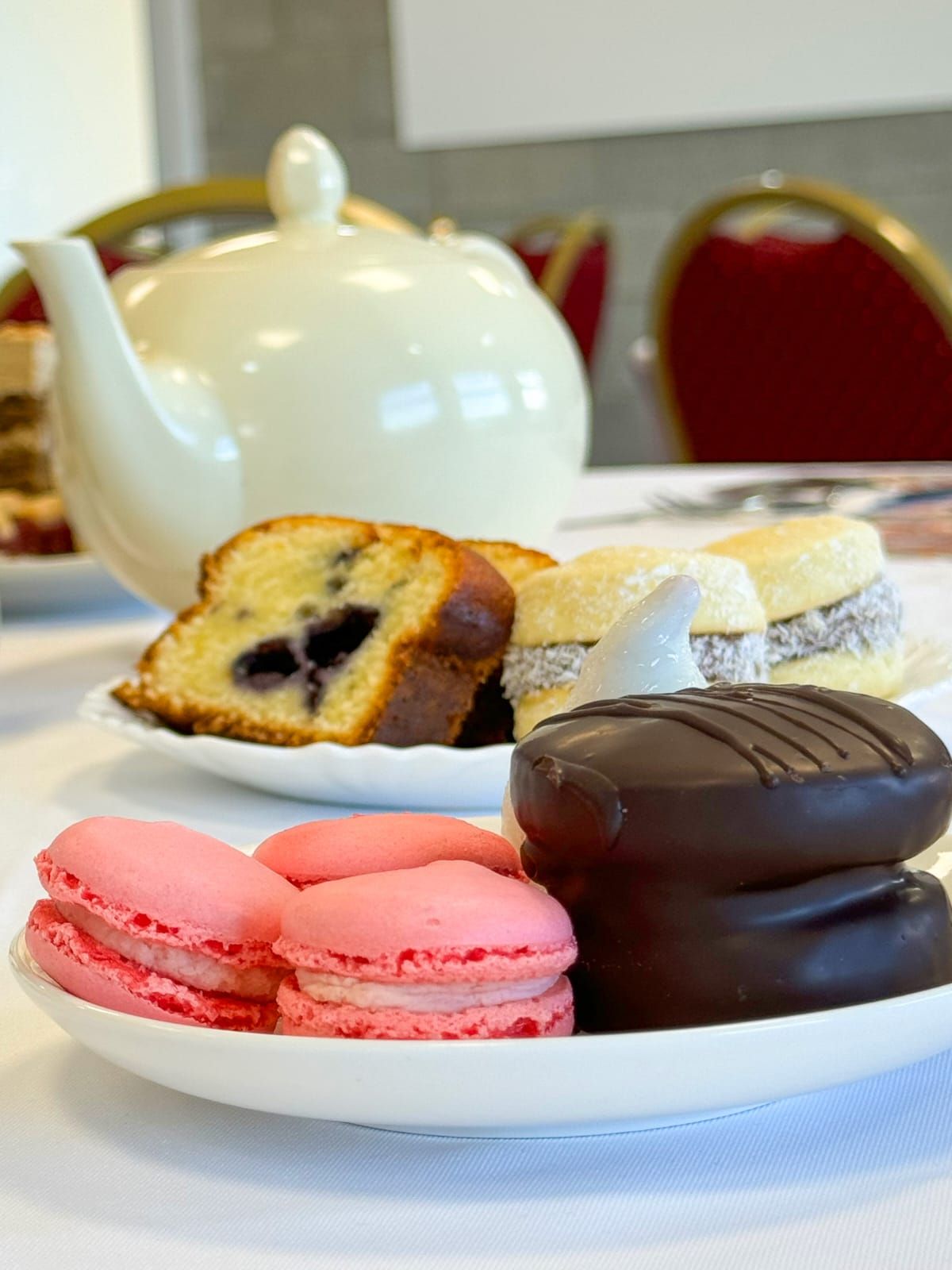 Un plato de macarons reposa sobre una mesa junto a una tetera.