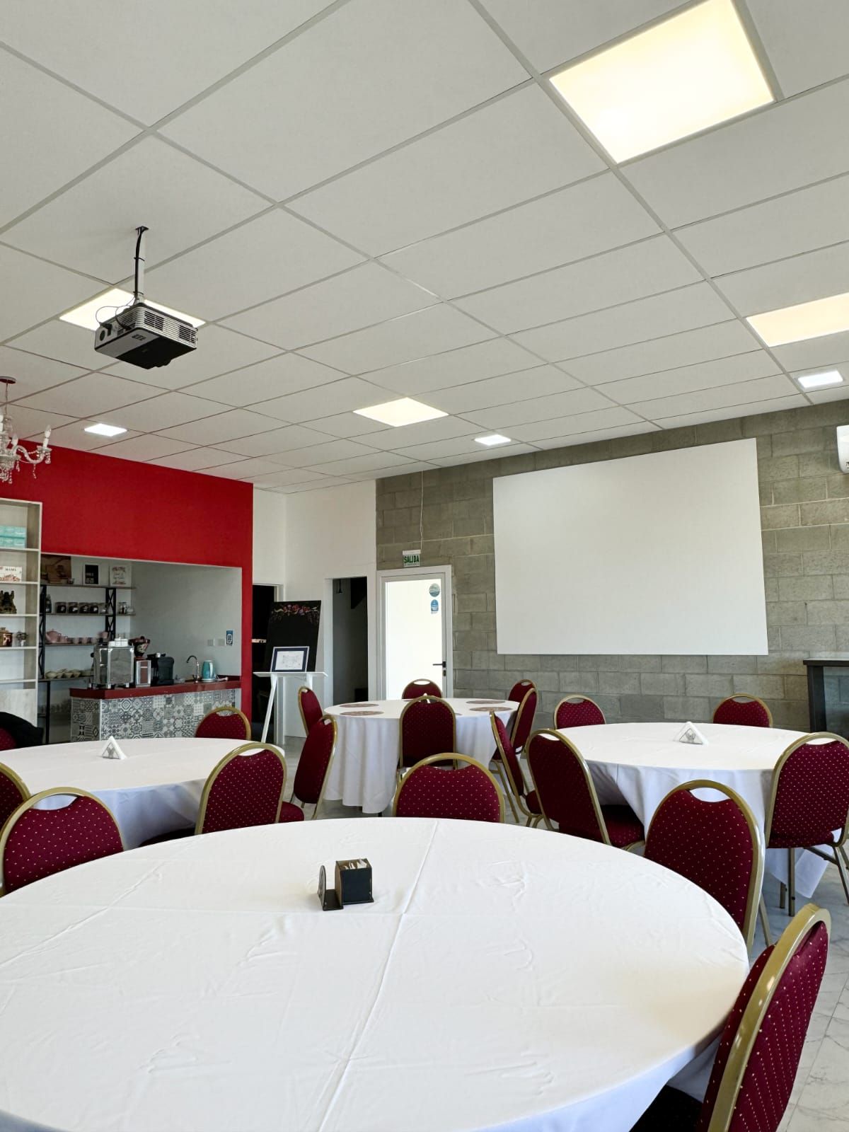 Una sala grande con mesas y sillas y un proyector en el techo.