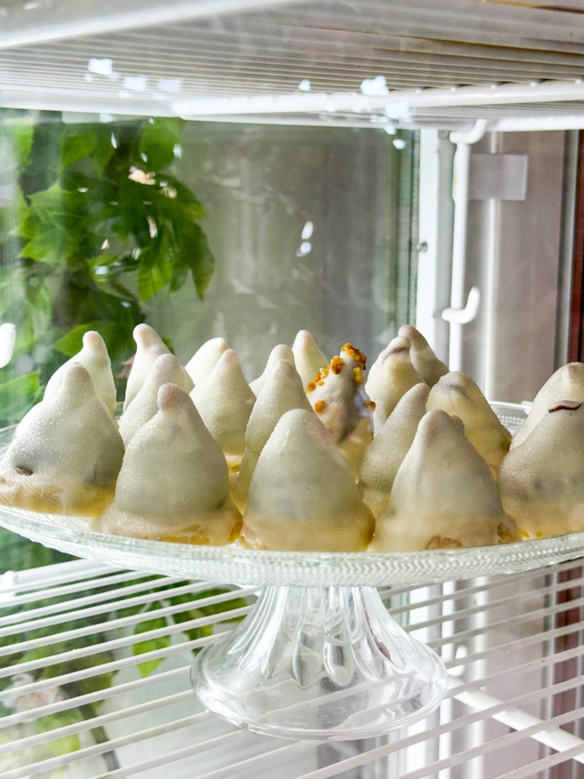Un plato de vidrio lleno de galletas cubiertas de chocolate blanco en un estante.