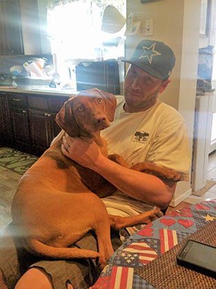 A Man Is Sitting at A Table Holding a Vizsla Dog.