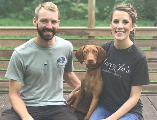 A Man and A Woman Are Sitting on A Bench with A Vizsla Dog.