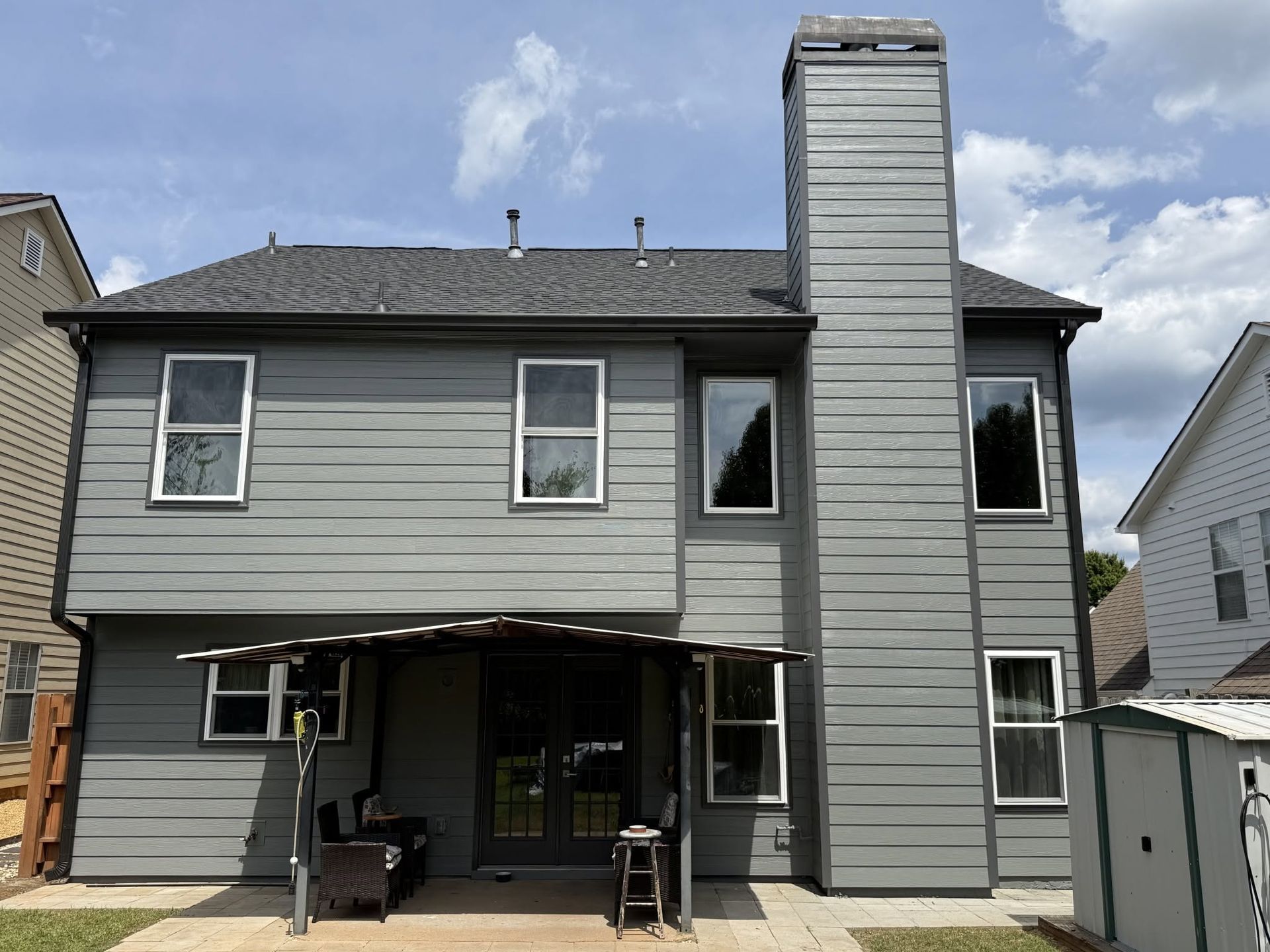 Gray two-story house with a tall chimney, covered patio, and attached garage under a cloudy sky