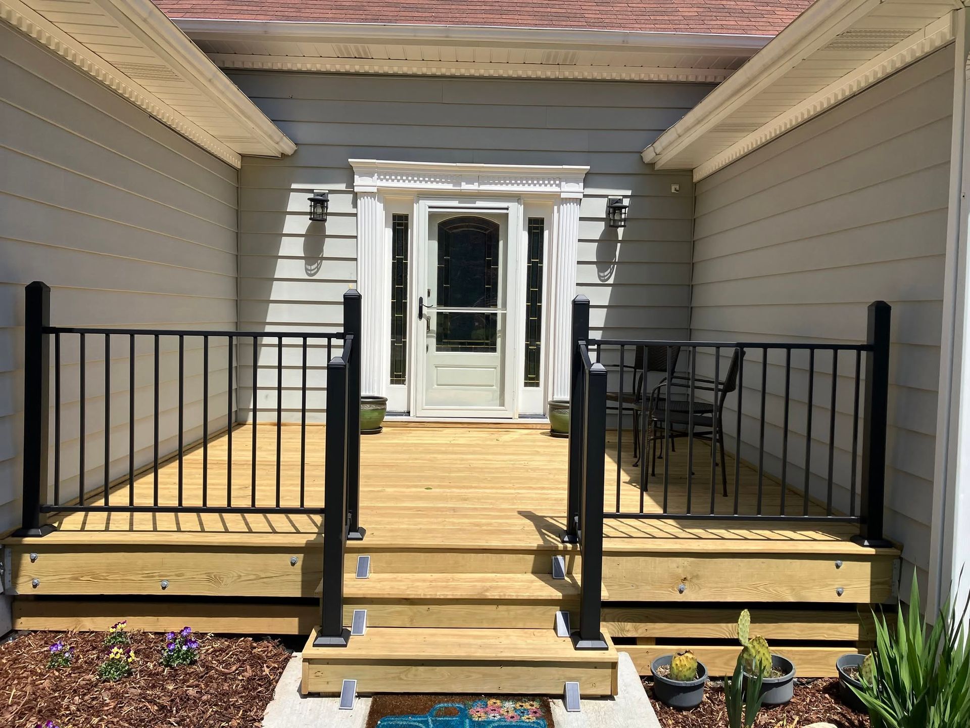 Front porch with wooden ramp, black railings, and white double doors at a gray house