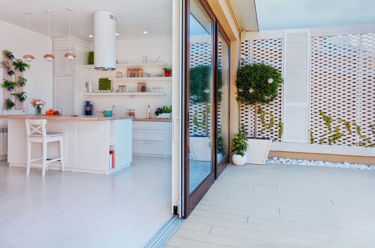 Bright modern kitchen opening to a sunlit patio with sliding glass doors and potted plants