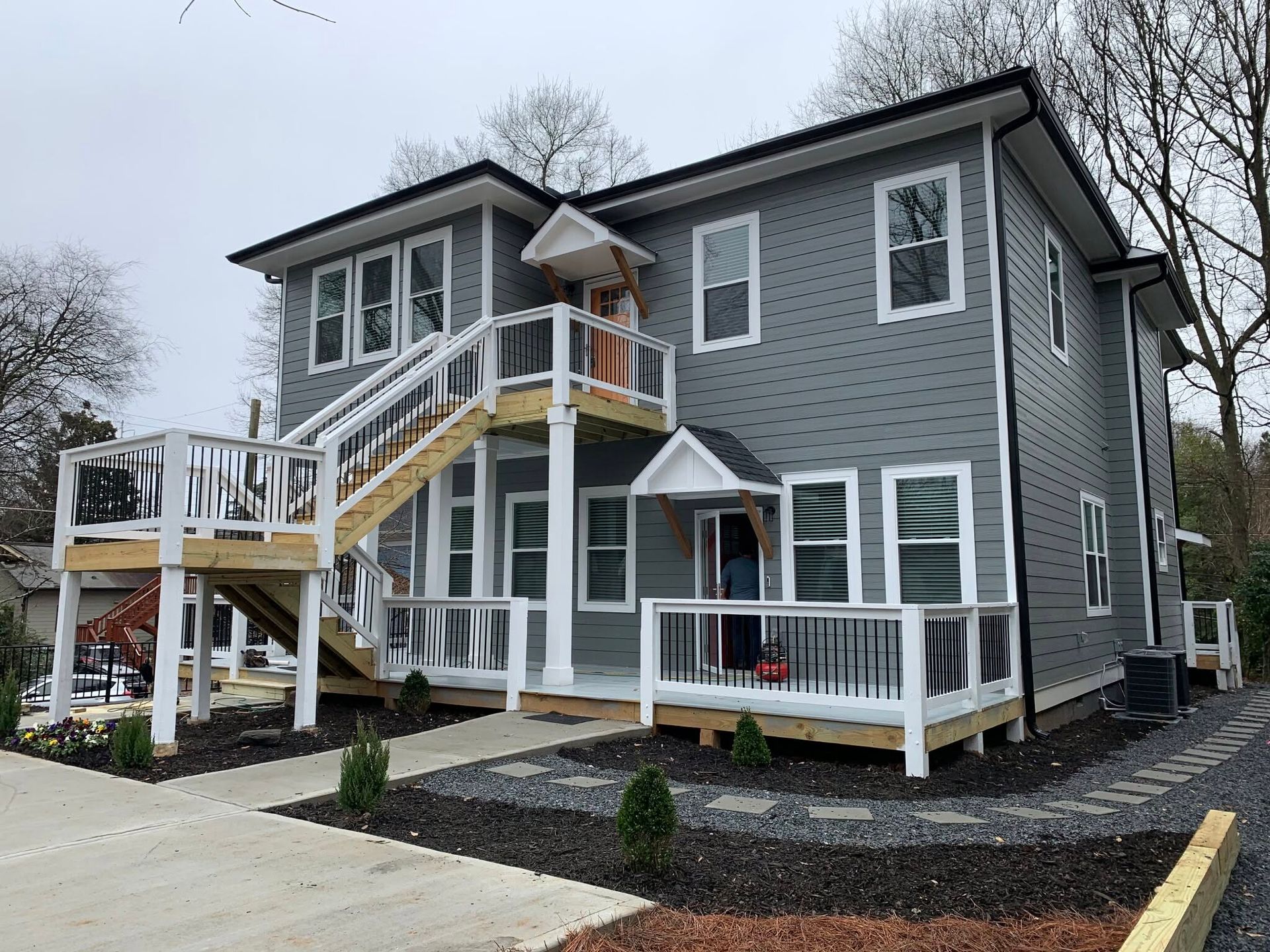 Gray two-story house with white trim, front porch, and exterior stairs on a snowy day