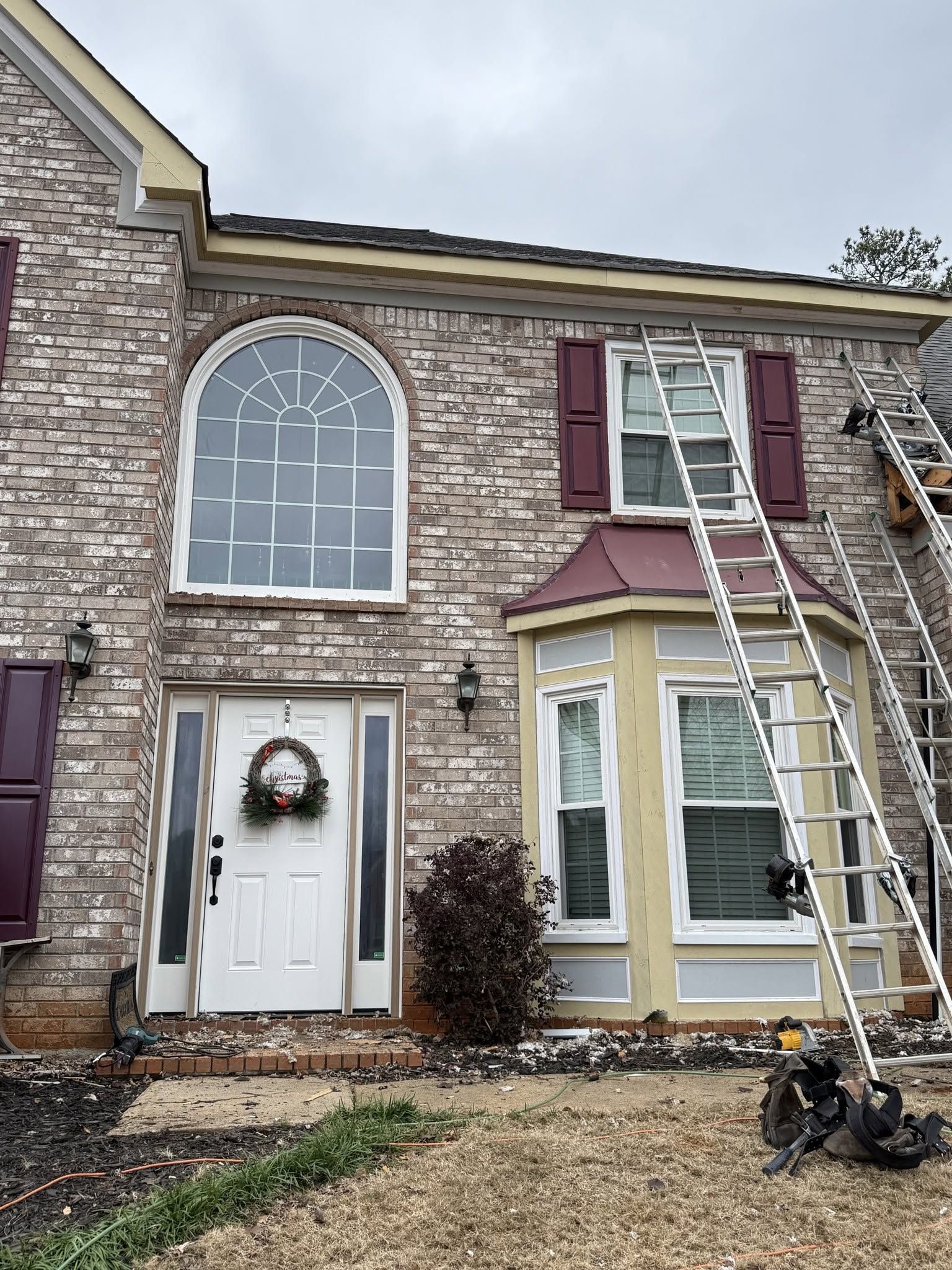 Two-story brick townhouse with white door and wreath; ladder leans against upper window during repairs