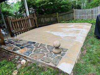 A concrete patio with a stone walkway and a wooden fence.