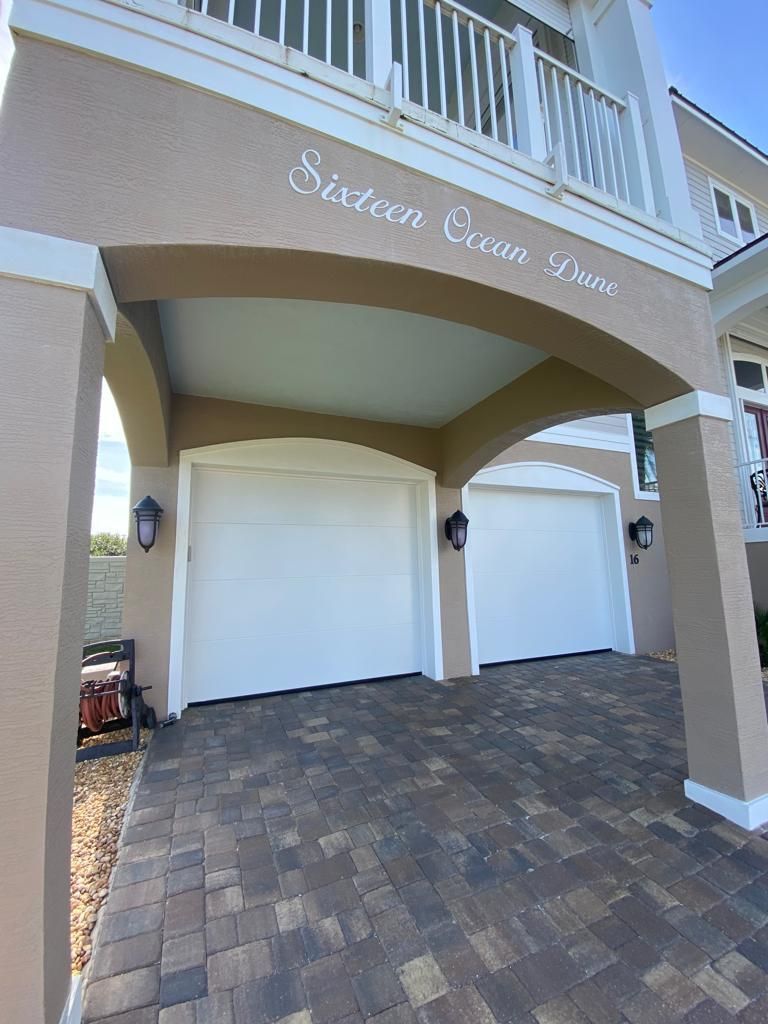 A house with three white garage doors and a brick driveway.