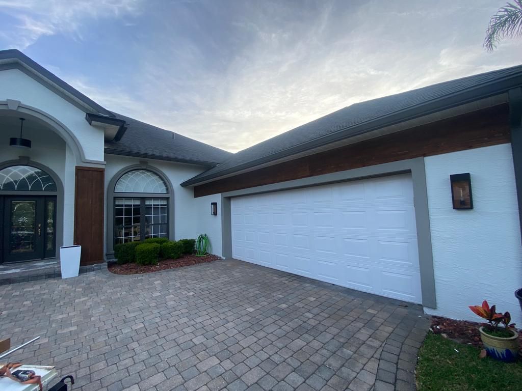 A white house with a large garage door and a brick driveway.