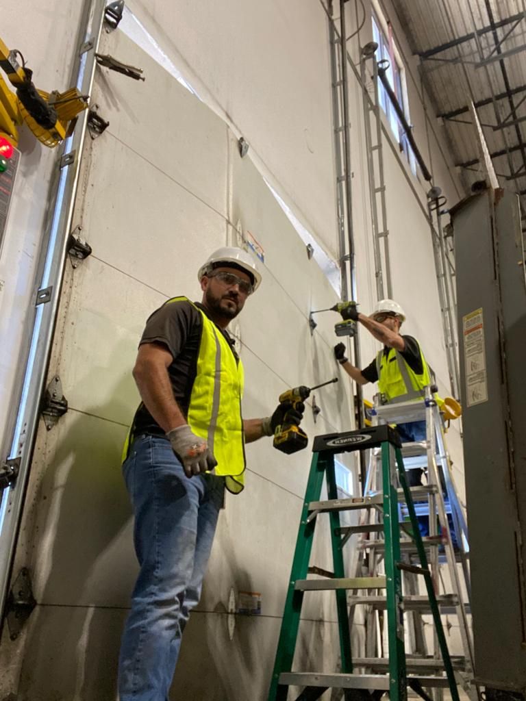 Two men are working on a garage door in a building.
