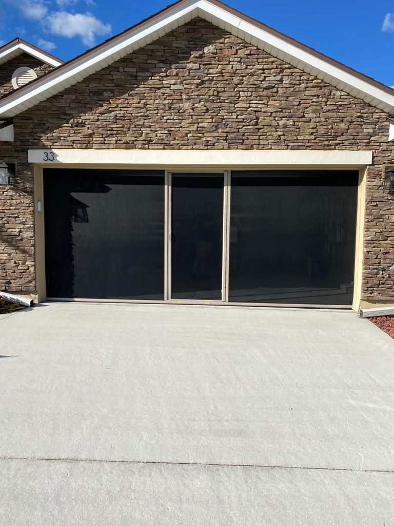 A brick house with a screened in garage door and a driveway.