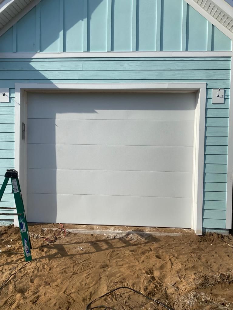A white garage door is sitting in front of a blue house.
