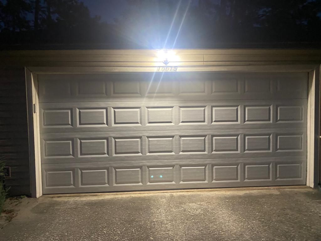 A garage door with a light on it is open at night.