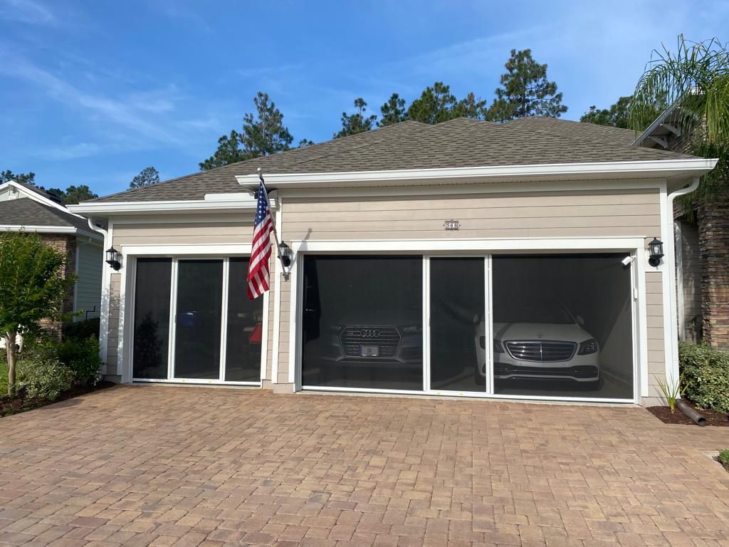 A car is parked in front of a house with a screened in garage door.