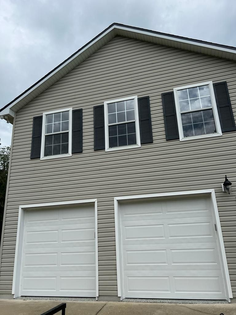 A house with two garage doors and black shutters on the windows.