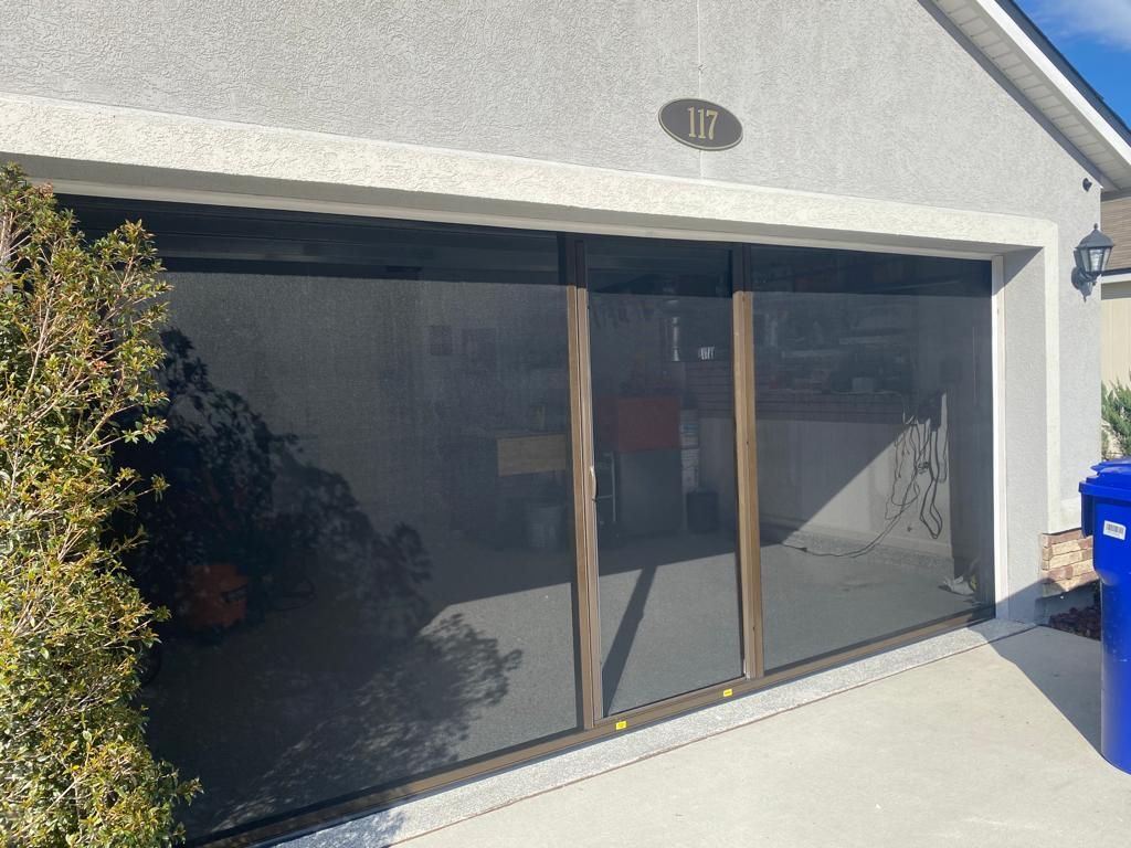 A garage with a screen door and a trash can in front of it.