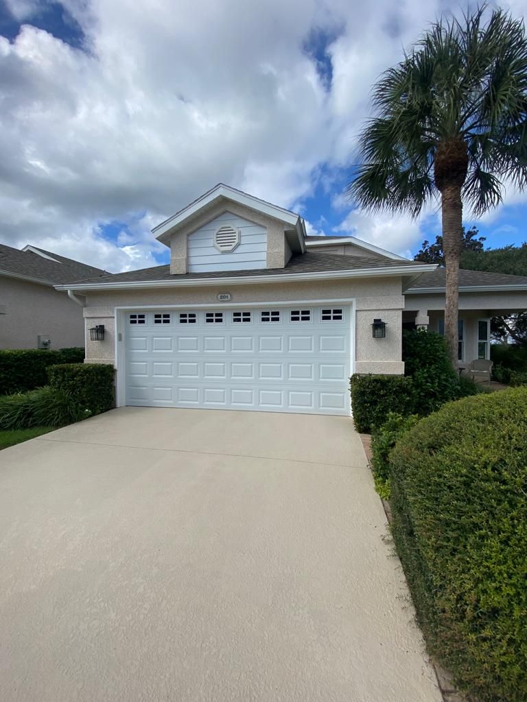 A house with a white garage door and a palm tree in front of it.