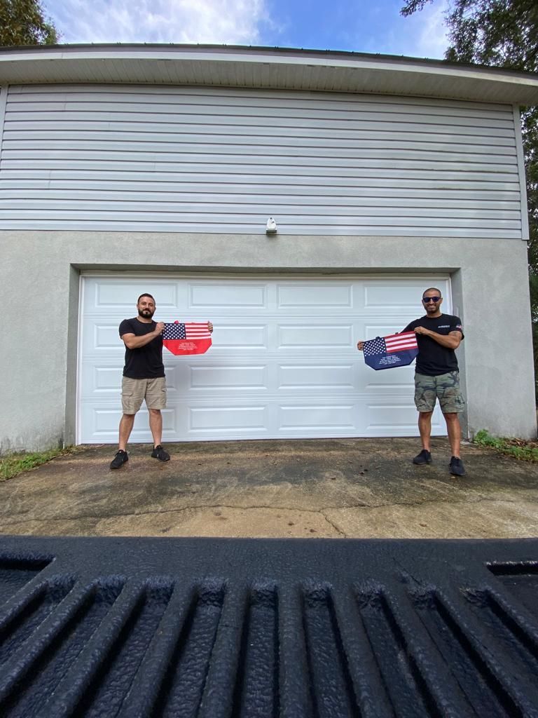 Two men are standing in front of a garage holding american flags.