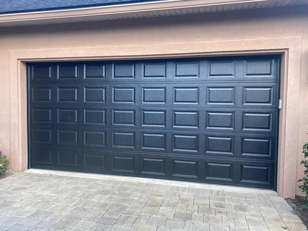 A black garage door is sitting on top of a brick driveway.