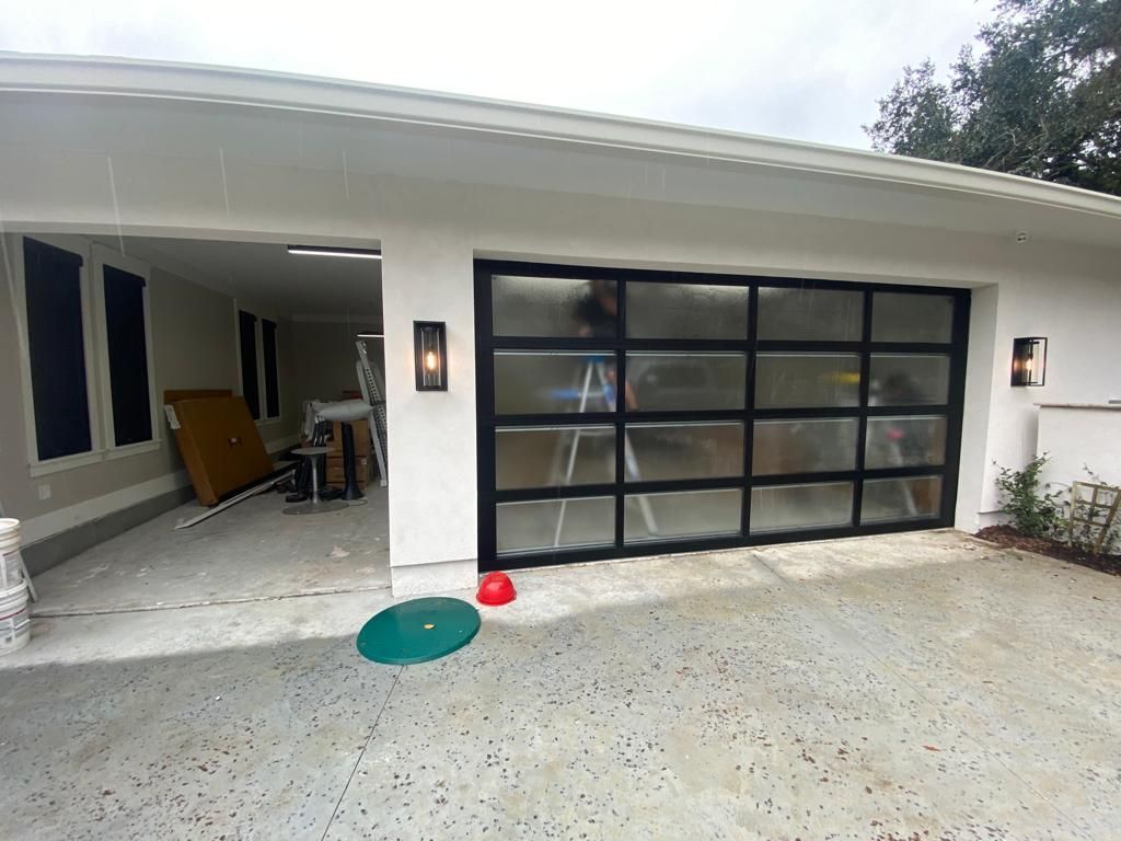 A man is standing in front of a white house with a black garage door.